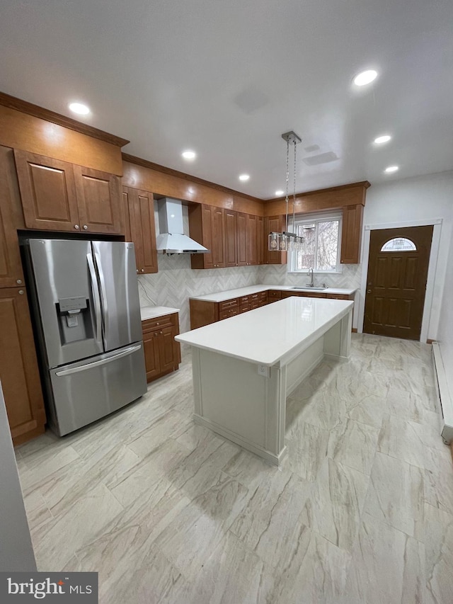 kitchen featuring sink, hanging light fixtures, wall chimney exhaust hood, stainless steel fridge, and a kitchen island