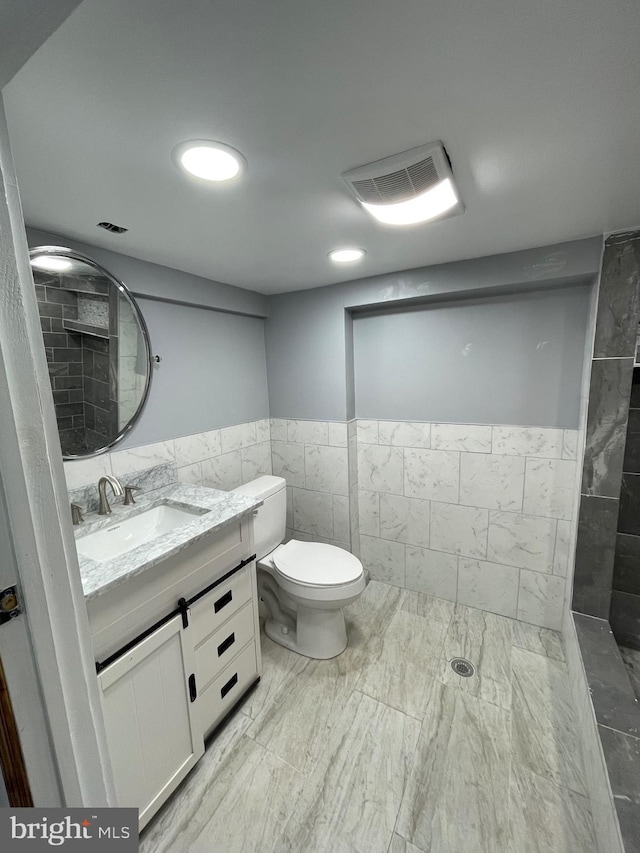 bathroom with a tile shower, vanity, tile walls, and toilet