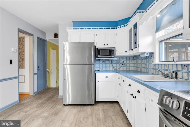 kitchen featuring light wood-type flooring, backsplash, stainless steel appliances, sink, and white cabinets