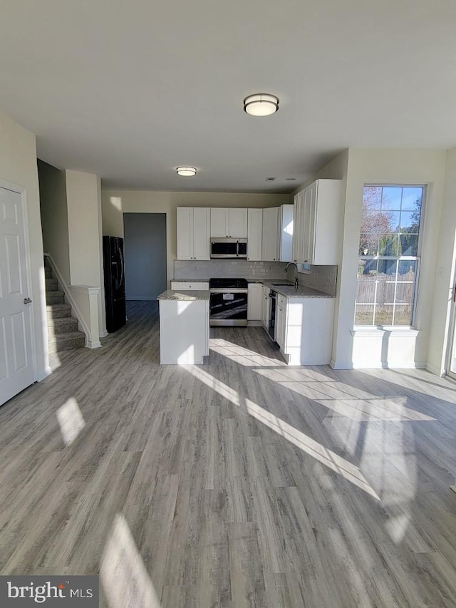 kitchen with appliances with stainless steel finishes, a kitchen island, sink, light hardwood / wood-style flooring, and white cabinetry