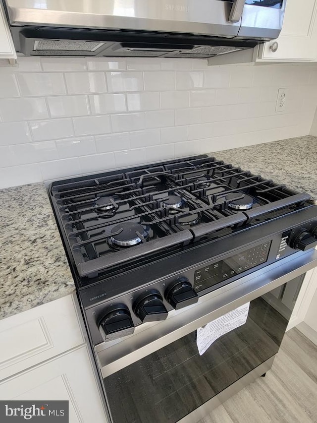 room details with white cabinets, light stone countertops, backsplash, and stainless steel stove