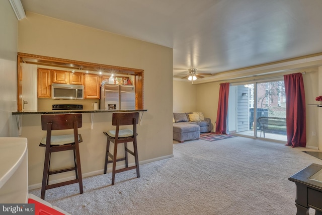 kitchen with light carpet, dark stone counters, a kitchen breakfast bar, ceiling fan, and stainless steel appliances