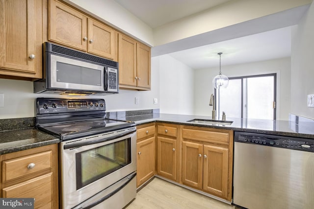 kitchen with kitchen peninsula, light wood-type flooring, dark stone counters, stainless steel appliances, and sink