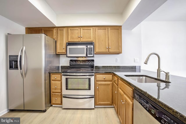 kitchen featuring light wood-type flooring, sink, appliances with stainless steel finishes, and dark stone counters