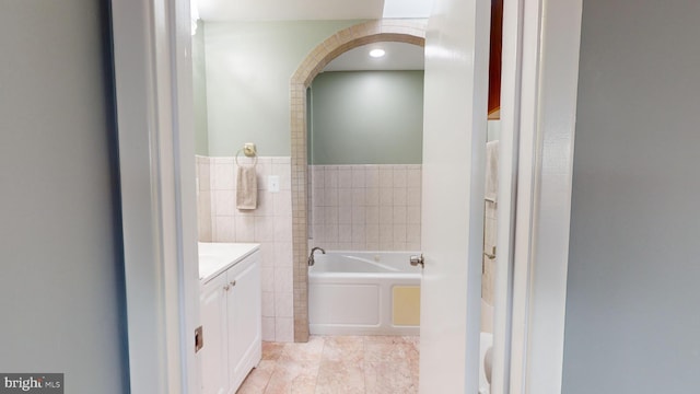 bathroom featuring a tub to relax in, tile patterned flooring, vanity, and tile walls