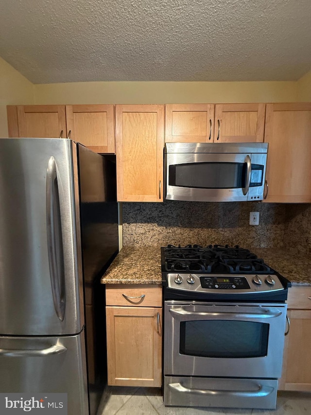 kitchen with tasteful backsplash, dark stone countertops, stainless steel appliances, and a textured ceiling