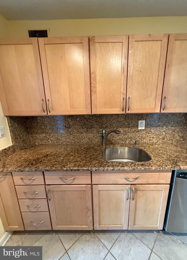 kitchen featuring light brown cabinets, sink, stainless steel dishwasher, dark stone countertops, and tasteful backsplash