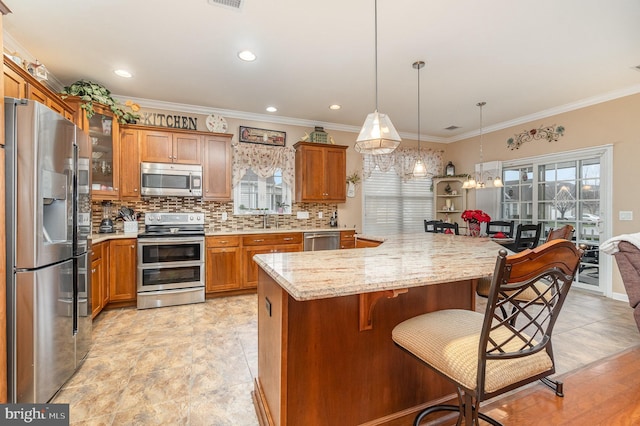 kitchen with light stone countertops, ornamental molding, stainless steel appliances, pendant lighting, and a breakfast bar area