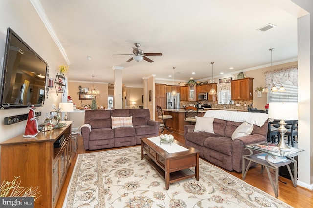 living room with ceiling fan with notable chandelier, light hardwood / wood-style floors, and crown molding