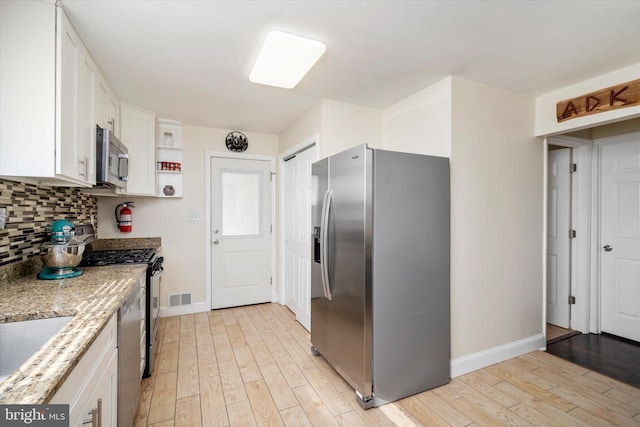 kitchen with white cabinets, light stone counters, appliances with stainless steel finishes, and light hardwood / wood-style flooring