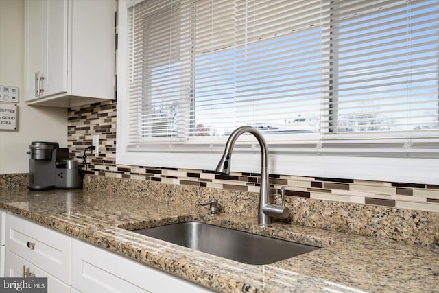 kitchen with decorative backsplash, white cabinetry, sink, and stone countertops