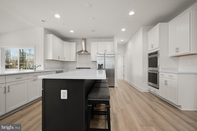 kitchen with white cabinets, a center island, wall chimney exhaust hood, and appliances with stainless steel finishes