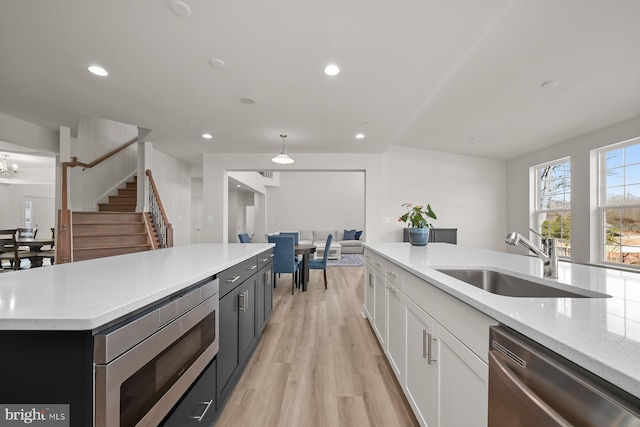 kitchen with white cabinetry, sink, stainless steel appliances, a kitchen island, and light wood-type flooring