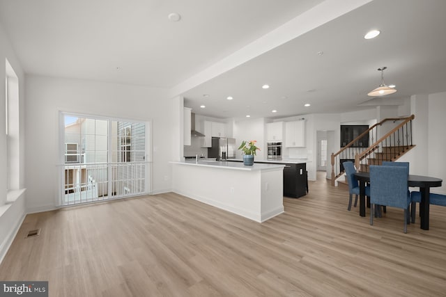 kitchen with stainless steel appliances, light hardwood / wood-style flooring, kitchen peninsula, decorative light fixtures, and white cabinets