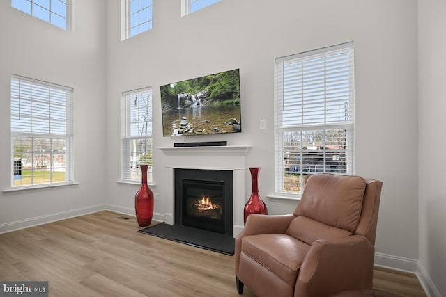 living area featuring a towering ceiling, light wood-type flooring, and plenty of natural light