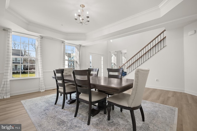 dining area with an inviting chandelier, light hardwood / wood-style flooring, a raised ceiling, and ornamental molding