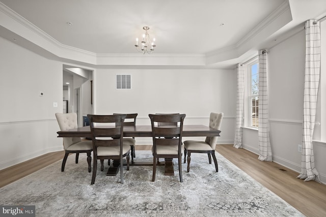 dining room featuring a tray ceiling, crown molding, light hardwood / wood-style flooring, and an inviting chandelier