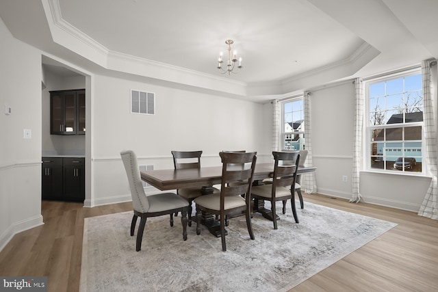 dining area with a raised ceiling, ornamental molding, light hardwood / wood-style floors, and an inviting chandelier