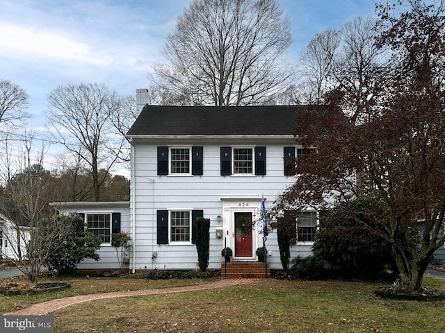 colonial home with entry steps, a front lawn, and a chimney