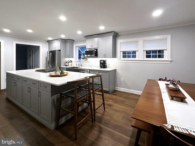 kitchen with gray cabinetry, stainless steel appliances, dark wood-type flooring, crown molding, and a center island