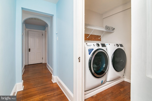 clothes washing area featuring dark wood-style floors, washing machine and dryer, arched walkways, and baseboards