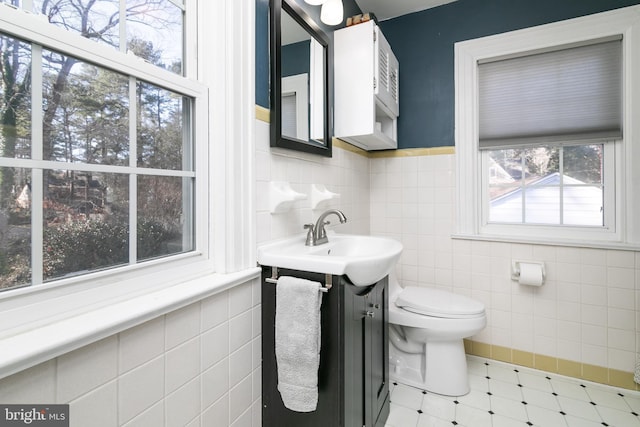 half bath with a wainscoted wall, tile walls, toilet, and vanity