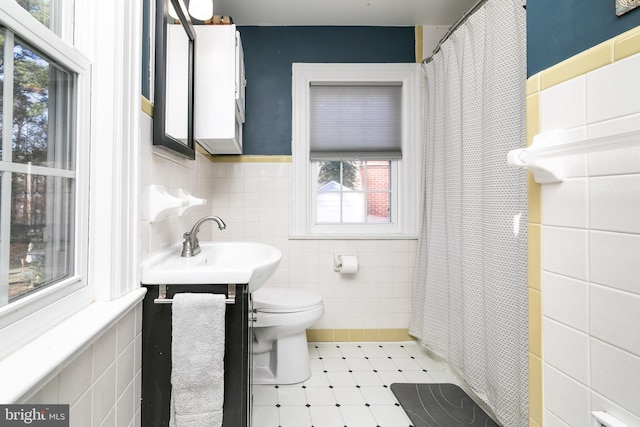 bathroom with tile walls, toilet, wainscoting, a sink, and a shower with curtain