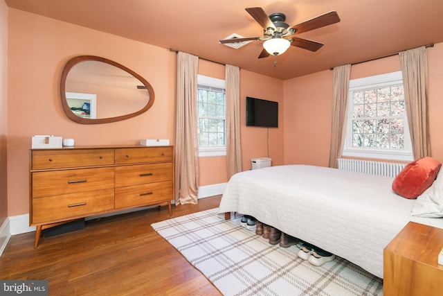 bedroom with dark wood-type flooring, radiator, baseboards, and a ceiling fan