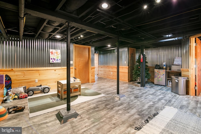 unfinished basement featuring fridge, metal wall, and wood finished floors