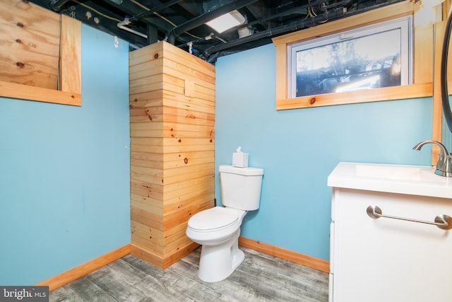 half bath with toilet, baseboards, a sink, and wood finished floors