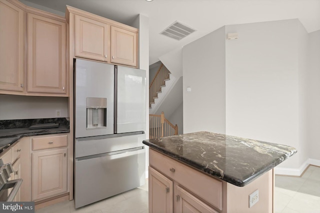 kitchen with dark stone countertops, light tile patterned floors, light brown cabinetry, a kitchen island, and stainless steel fridge with ice dispenser