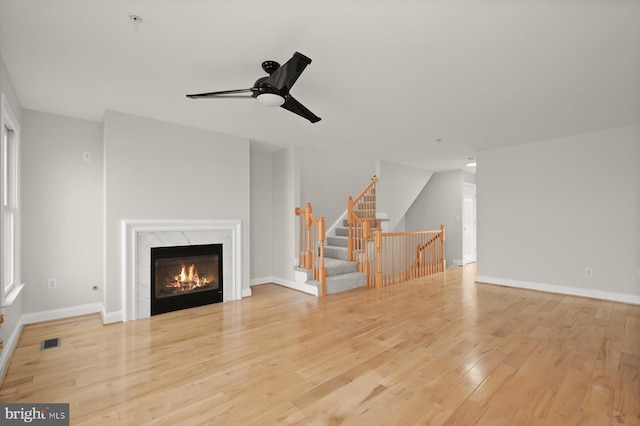 unfurnished living room featuring ceiling fan, a premium fireplace, and light hardwood / wood-style flooring