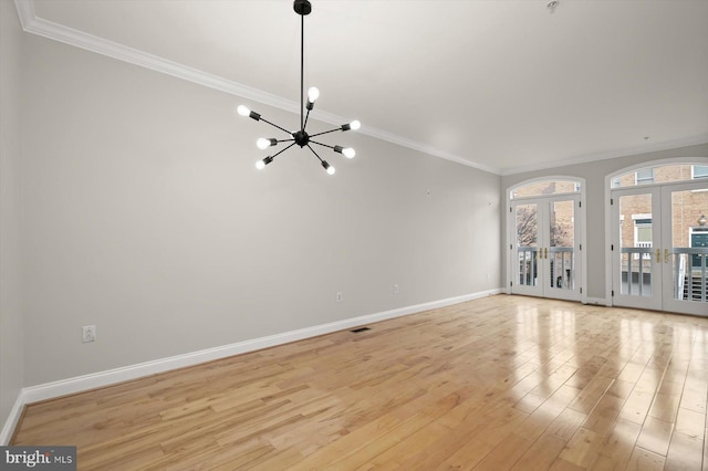 unfurnished living room with a notable chandelier, light wood-type flooring, crown molding, and french doors