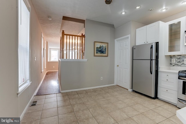 kitchen featuring tasteful backsplash, white cabinetry, light tile patterned floors, and stainless steel appliances