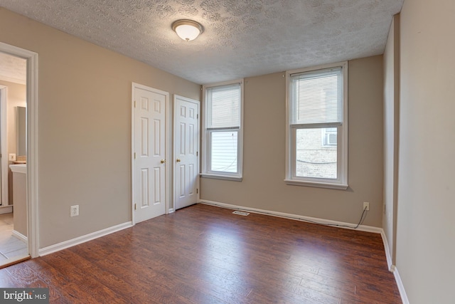 unfurnished bedroom featuring dark hardwood / wood-style flooring, a textured ceiling, and ensuite bath