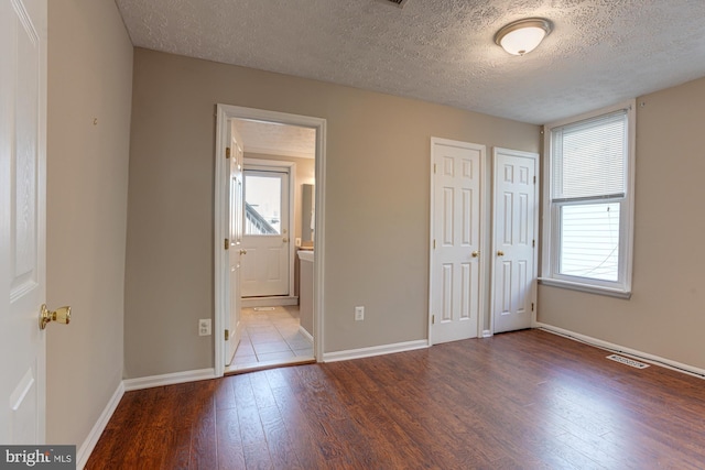 unfurnished bedroom featuring ensuite bathroom, dark wood-type flooring, and a textured ceiling