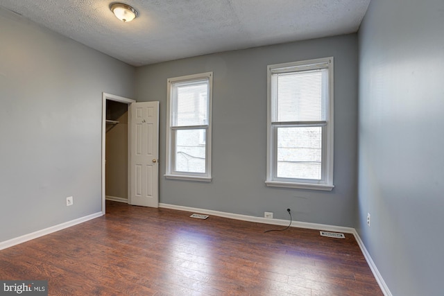 unfurnished bedroom with a textured ceiling, a closet, and dark wood-type flooring