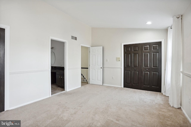 unfurnished bedroom featuring ensuite bath, light carpet, a closet, and vaulted ceiling