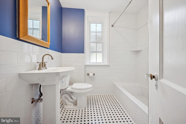 bathroom featuring tile patterned floors, tiled shower / bath combo, toilet, and tile walls