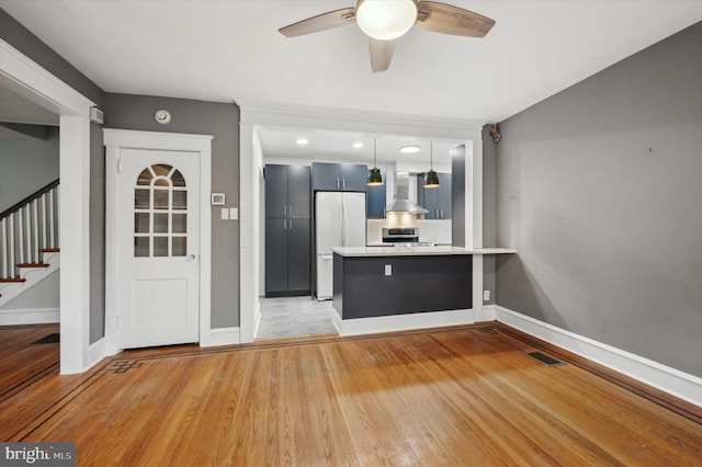 kitchen featuring wall chimney range hood, white refrigerator, kitchen peninsula, stove, and pendant lighting