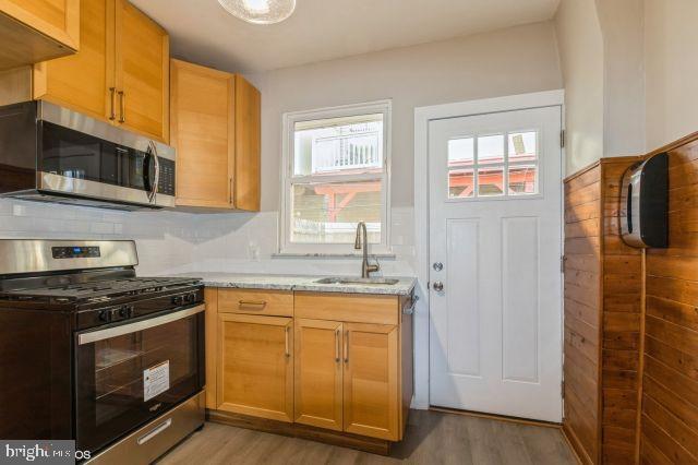 kitchen with light stone countertops, appliances with stainless steel finishes, light hardwood / wood-style floors, and sink