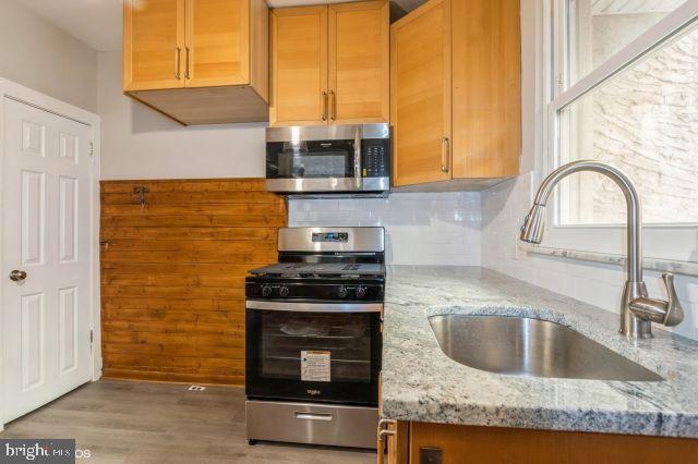 kitchen with appliances with stainless steel finishes, light wood-type flooring, backsplash, light stone counters, and sink