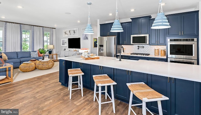 kitchen with blue cabinets, pendant lighting, decorative backsplash, a breakfast bar, and appliances with stainless steel finishes