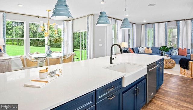 kitchen with sink, stainless steel dishwasher, blue cabinets, pendant lighting, and hardwood / wood-style flooring