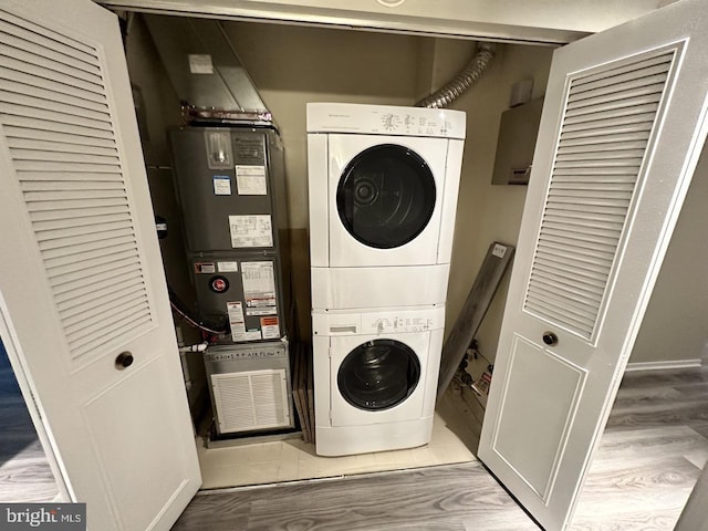 clothes washing area with stacked washer / dryer, heating unit, and hardwood / wood-style floors