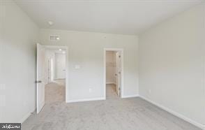 unfurnished bedroom featuring a walk in closet and light colored carpet