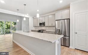 kitchen with appliances with stainless steel finishes, decorative light fixtures, light hardwood / wood-style floors, and an island with sink