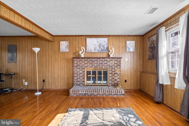 unfurnished living room featuring crown molding, wood-type flooring, wooden walls, and a brick fireplace