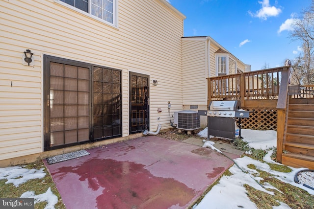 snow covered patio with a wooden deck, central AC unit, and grilling area