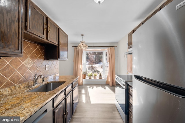 kitchen featuring sink, appliances with stainless steel finishes, hanging light fixtures, light stone counters, and decorative backsplash